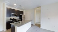 This single-floor residence in Diamond offers a thoughtfully designed open-concept layout that seamlessly connects the kitchen and living areas. The kitchen is a standout feature, equipped with stainless steel appliances including a refrigerator, range, and microwave. Rich dark cabinetry provides ample storage and contrasts elegantly with the granite countertops that extend across both the perimeter counters and a central island with a built-in sink — ideal for meal preparation and casual dining. Recessed lighting throughout the kitchen ensures a well-lit, functional workspace.

The living area is bathed in natural light, courtesy of a set of French doors that open to a private outdoor balcony, creating a seamless indoor-outdoor connection. The neutral carpeting and soft, cream-toned walls lend the space a clean and welcoming ambiance. A hallway off the main living area leads to additional rooms, with multiple doors suggesting well-defined private spaces within the residence. The overall design emphasizes a modern yet understated aesthetic, with quality finishes and an efficient use of space throughout.