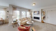 This single-floor residence offers a thoughtfully designed layout that balances comfort and style throughout. The living room serves as a welcoming centerpiece, bathed in natural light from a generous bank of windows dressed with sheer, patterned curtains. Soft carpeting, a sleek wall-mounted electric fireplace, and a mounted television contribute to the room's relaxed yet refined atmosphere.

The kitchen is both functional and visually appealing, featuring soft blue-grey cabinetry paired with marble-look countertops and a matching island with seating. Stainless steel appliances — including a French door refrigerator, electric range, and over-the-range microwave — are complemented by a classic subway tile backsplash and light wood-look tile flooring, creating a clean, contemporary aesthetic.

The bedrooms are carpeted and well-lit, each equipped with a ceiling fan and windows that invite natural light and outdoor views. The primary bedroom offers ample space with room for a full bedroom suite, while additional bedrooms provide comfortable, versatile accommodations.

The bathroom continues the home's cohesive design with grey cabinetry, marble-look countertops, a wide vanity mirror, and a modern multi-bulb light bar. Decorative tilework on the floor adds a charming finishing touch. Throughout, the space maintains a warm, neutral palette that creates a welcoming and livable environment.