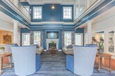 Located at 155 Sterling Manor Drive in Williamsburg, Virginia, this two-story community clubhouse offers a well-appointed gathering space designed with classic architectural details and a cohesive, elegant aesthetic throughout.

The entry foyer welcomes visitors with large-pane windows that flood the space with natural light, rich tile flooring, and a striking hardwood staircase with white spindle railings and dark wood newel posts. The upper level features an open hallway with gleaming hardwood floors, decorative columns with ornate capitals, and coffered ceiling details that lend an air of refinement.

The main lounge area is a standout, boasting soaring ceilings accented with bold teal upper walls, a classic white fireplace flanked by large windows, and comfortable seating — making it an inviting retreat. Adjacent to the lounge, a dedicated fitness center provides ample space for cardio equipment, strength machines, and a mirrored studio area with a ballet barre. A separate weight room offers additional workout equipment on durable rubber flooring.

The dining area features a tray ceiling with teal accents, wainscoting, and multiple seating arrangements suited for both casual gatherings and organized events. The full kitchen is equipped with white cabinetry, subway tile backsplash, a center island with a sink, and stone tile flooring — ideal for community functions. A game room with a billiard table completes the offering, rounding out this comprehensive and beautifully designed community facility.
