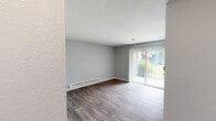 Located on the ground floor in Lakewood, WA, this well-appointed one-bedroom, one-bathroom unit offers a comfortable and functional layout. The living area features durable hardwood-style flooring, neutral gray walls, and a baseboard heating system. A sliding glass door with vertical blinds fills the space with natural light and opens to a pleasant outdoor view, creating an inviting atmosphere.

The kitchen is thoughtfully updated with gray shaker-style cabinetry, crisp white countertops, and black appliances including an electric range and refrigerator. A large window above the counter brings in additional natural light, and ample cabinet space provides generous storage. The kitchen flows efficiently into the rest of the unit.

The bedroom is a comfortable, well-proportioned room with soft carpeting, a window with blinds, a baseboard heater, and a sliding-door closet offering practical built-in storage. The bathroom includes a full tub-shower combination with a curved curtain rod, a toilet, and a vanity, finished with clean, neutral tones.

Throughout the unit, the consistent color palette of soft grays and whites creates a cohesive, modern feel. The textured ceilings and clean white trim add subtle architectural detail, making this a practical and attractive space in the Lakewood community.