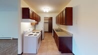 Located at 1100 County Road D W in New Brighton, Minnesota, this single-floor unit offers a practical and well-organized layout suited for comfortable everyday living. The galley-style kitchen is a functional centerpiece, featuring rich dark wood cabinetry lining both walls, light-toned countertops, a double sink, tile flooring, and white appliances including an electric range and refrigerator. A closet at the end of the kitchen provides additional storage convenience.

The living area is generously proportioned, finished with wall-to-wall carpeting and neutral white walls. A large window dressed with vertical blinds allows ample natural light to fill the space, while a ceiling fan adds to the room's comfort. Baseboard heating runs along the perimeter, providing efficient climate control throughout.

The bedroom is carpeted and well-sized, offering a built-in closet with sliding doors and a dedicated vanity area with sink and cabinetry — a practical feature that adds functionality. A window unit air conditioner and baseboard heater ensure year-round comfort, and vertical blinds on the window allow for adjustable natural light.

The bathroom is clean and bright, featuring a full tub and shower combination, a white vanity, toilet, and classic mosaic tile flooring with a subtle geometric accent pattern. Dark wood doors throughout the unit add a warm, cohesive design element.
