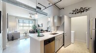 This thoughtfully designed one-bedroom, one-bathroom unit showcases a distinctive urban loft aesthetic, blending industrial character with modern comfort across a single floor. The open-concept living area immediately impresses with soaring ceilings, exposed ductwork, and polished concrete floors that reflect natural light pouring in through large grid-pane windows. The combined living and dining area offers a spacious, airy feel with a ceiling fan overhead and city views beyond.

The kitchen features a peninsula with a white quartz countertop and seating for two, complemented by gray cabinetry, stainless steel appliances, a built-in dishwasher, and pendant lighting—seamlessly connecting to the main living space.

The generously sized bedroom provides a calm retreat with soft neutral tones, a large window with outdoor views, a ceiling fan, and access to a walk-in closet outfitted with wire shelving and hanging rods. The full bathroom offers a marble-tiled tub and shower surround, gray vanity cabinetry with gold hardware, and polished concrete flooring. A dedicated in-unit laundry area with a full-size washer and dryer rounds out this well-appointed, functionally complete residence.