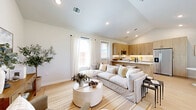 Located at 15883 Bear Trap Way in Frisco, TX, this model home presents a carefully crafted single-story layout that maximizes both functionality and style. The open-concept living room features vaulted ceilings, recessed lighting, and light wood-style flooring that flows throughout the main living areas, creating a bright and airy atmosphere enhanced by sheer white curtains and abundant natural light.

The kitchen is a standout feature, showcasing contemporary flat-panel cabinetry in a warm wood-grain finish, white quartz countertops, stainless steel appliances, and a central island with bar seating — ideal for both cooking and casual dining. Subtle under-cabinet lighting adds warmth to the space.

The primary bedroom is a serene retreat with plush carpeting, a ceiling fan, and large windows that invite natural light and outdoor views. It connects seamlessly to a well-designed en-suite bathroom featuring wood-toned vanity cabinetry, a dual sink, and clean, neutral finishes. A dedicated closet provides additional storage.

A second bathroom serves the remaining areas of the home. Throughout the space, a cohesive neutral palette, modern fixtures, and quality materials combine to deliver a polished, contemporary living environment in one of Frisco's vibrant communities.