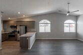 This single-story home on Olive Street in Hesperia, California presents a well-designed layout with contemporary finishes throughout. The open-concept living and dining area is anchored by vaulted ceilings that lend an airy, expansive feel, complemented by wood-look plank flooring and neutral toned walls. A ceiling fan overhead and an arched window allow natural light to fill the space generously.

The kitchen is appointed with dark-stained cabinetry, granite countertops, and a full suite of stainless steel appliances, including a gas range, built-in microwave, refrigerator, and dishwasher. A peninsula counter connects the kitchen to the living area, making it well-suited for both everyday use and entertaining.

The bedrooms feature plush carpet flooring, vaulted ceilings, ceiling fans, and sliding glass door access to the exterior. Walk-in closets with built-in shelving and hanging rods provide organized storage. Both bathrooms include granite-topped vanities with dark wood cabinetry and hardwood-style flooring, with one bathroom offering a shower-tub combination.

The attached garage features a concrete floor and an automatic opener, offering ample storage and parking capacity.