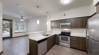 This thoughtfully designed 1-bedroom, 1-bathroom unit offers a comfortable and functional layout across a single floor. The open-concept kitchen is a standout feature, showcasing dark espresso cabinetry, light quartz countertops, a peninsula with pendant lighting, and a full suite of stainless steel appliances including a refrigerator, electric range, microwave, and dishwasher. Wood-look flooring runs throughout the main living areas, adding warmth and continuity to the space.

The living area is bright and inviting, benefiting from natural light through windows that frame views of lush greenery and a pool area. A ceiling fan provides additional comfort, while a glass-panel exterior door enhances the connection to the outdoors.

The bedroom is a well-proportioned retreat finished with plush carpet, a ceiling fan with light fixture, and a window that brings in natural light and outdoor views. A dedicated closet provides convenient storage.

The bathroom features a dark wood vanity with light countertop, a large mirror, and clean, neutral finishes throughout. A separate dedicated laundry room houses a full-size Whirlpool front-load washer and dryer with overhead shelving, adding exceptional practicality to everyday living.