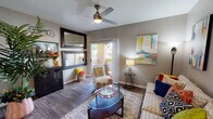 This single-floor residence offers a thoughtfully designed layout that balances comfort and style throughout. The living room serves as the heart of the home, featuring rich wood-look flooring, a contemporary ceiling fan, and a sliding glass door that opens to a private patio, filling the space with natural light and outdoor views. Colorful abstract artwork and large decorative mirrors add visual depth and personality to the neutral gray walls.

The kitchen is efficiently designed with medium-toned wood cabinetry, light countertops, a breakfast bar peninsula, and black appliances including a refrigerator, range, and microwave. A window above the sink allows natural light to brighten the workspace. Adjacent to the kitchen, the dining area features stylish globe pendant lighting, a large framed mirror, and wood-look flooring that flows seamlessly throughout the common areas.

The bedroom is a calm retreat, carpeted for comfort and outfitted with a ceiling fan, sheer window treatments that invite soft light, and access to a walk-in closet. Bold floral artwork in purple tones adds a striking focal point above the bed. The bathroom is finished with wood-look flooring, a shower-tub combination, and clean, neutral finishes throughout.