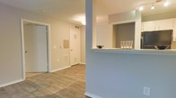 This single-floor residence offers a clean, functional layout designed for comfortable everyday living. The interior is finished with warm hardwood-style flooring that runs throughout, providing a cohesive and welcoming aesthetic across the space.

A standout architectural feature is the pass-through counter that connects the kitchen to the adjacent living area, topped with a light-colored surface and accented by a soft blue wall — a charming detail that adds character while maintaining an open, communicative flow between spaces.

The entryway and hallway are well-proportioned, offering clear sightlines through the unit. Neutral, warm-toned walls contribute to a bright and airy atmosphere, complemented by ceiling-mounted lighting that ensures consistent illumination throughout.

Practical built-in features are evident, including HVAC vents integrated into both the walls and floors, ensuring efficient climate control. A utility panel is also conveniently accessible within the hallway area. White trim and door frames provide crisp contrast against the warm wall tones, lending a polished, finished look to the interior.

Overall, the space strikes a balance between simplicity and thoughtful design, making it a practical and inviting single-floor home.