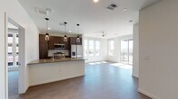 This single-floor residence showcases a contemporary design with a thoughtful, open layout. The kitchen is a standout feature, outfitted with dark wood cabinetry accented by matte black hardware, stone-look countertops, and a full suite of stainless steel appliances including a side-by-side refrigerator, range, and microwave. A peninsula with an undermount sink and pendant lighting above provides both additional workspace and a natural dividing point between the kitchen and the living area.

The living area is bright and airy, benefiting from large windows and a sliding glass door that opens to a private balcony with outdoor views. Ceiling fans are present in both the living area and bedroom, contributing to comfort throughout. The bedroom features soft carpeting, a ceiling fan, and a generous window that fills the room with natural light.

Two bathrooms serve the unit, each finished with stone-topped vanities, undermount sinks, and wood-toned cabinetry. One bathroom includes a glass-enclosed walk-in shower with tile surround. Throughout the unit, durable tile and luxury vinyl flooring complement the clean, neutral color palette, creating a cohesive and modern ambiance.