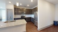 Located at 404 Gallop Ln. in Charlotte, NC, this single-floor residence offers a well-designed layout with contemporary finishes throughout. The kitchen is a standout feature, showcasing rich dark cabinetry, granite countertops, a classic subway tile backsplash, stainless steel appliances including a refrigerator, range, and built-in microwave, and a peninsula with an undermount sink — all set atop warm hardwood-style flooring. Recessed and pendant lighting complete the space. The living area extends from the kitchen and features a sliding glass door with a roller shade, allowing natural light to flow in and providing access to an outdoor balcony. The bedrooms are generously proportioned, finished with plush carpeting and ceiling fans, with windows framing views of the surrounding neighborhood. The primary bedroom connects to an en-suite bathroom equipped with a glass-enclosed walk-in shower, granite vanity, and dark cabinetry, while a secondary full bathroom offers a tub-shower combination with the same quality finishes. A spacious walk-in closet with wire shelving provides ample storage. The dedicated in-unit laundry area accommodates a full-size washer and dryer with an overhead utility shelf, adding everyday convenience to this thoughtfully appointed residence.