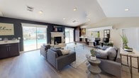 Located on Longfields Blvd in Great Mills, Maryland, this single-floor clubhouse facility offers a thoughtfully designed communal space with a range of functional and leisure-oriented features. The entrance welcomes visitors with a bright, open foyer accented by classic white columns, light hardwood-style flooring, and large windows that fill the space with natural light. A round dining table near the entry provides a welcoming meeting spot.

The main gathering area is expansive, featuring vaulted ceilings with recessed lighting and a striking stone fireplace as its focal point. A bold dark accent wall frames a wall-mounted television, while large sliding glass doors offer direct views of an outdoor pool area, seamlessly connecting interior and exterior spaces. Comfortable sectional seating and area rugs create a relaxed lounge atmosphere.

A dedicated workstation area with multiple desks and computers supports productivity needs. Adjacent to the lounge, a kitchenette includes dark cabinetry and modern appliances for resident use. A separate, fully equipped kitchen features rich espresso-toned shaker cabinets, stainless steel appliances, a mosaic tile backsplash, and light countertops, completing this versatile community space.