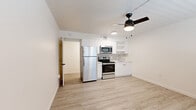 Located at 415 W Franklin St in Tucson, Arizona, this single-floor unit presents a clean, modern aesthetic throughout its thoughtfully designed layout. Light wood-look flooring flows consistently across the living and kitchen areas, creating a cohesive and bright interior.

The open kitchen is outfitted with stainless steel appliances, including a full-size refrigerator, electric range, and built-in microwave. White cabinetry with open shelving extends to the ceiling, complemented by a grey tile backsplash and light countertops that contribute to the kitchen's contemporary feel. A ceiling fan with an integrated light fixture serves the main living area, which also features a wall-mounted PTAC heating and cooling unit and a window fitted with white horizontal blinds for natural light control.

The bathroom maintains the unit's clean design language, featuring a white vanity with drawers, a black-framed mirror, and wood-look flooring that ties back to the rest of the unit. A dedicated laundry area houses a stacked GE washer and dryer unit, adding everyday convenience. Throughout, the white walls and neutral finishes create a fresh, move-in-ready environment.