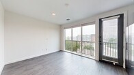This efficient yet thoughtfully designed one-bedroom, one-bathroom residence offers a clean, modern aesthetic throughout its single-floor layout. The entry hallway is lined with bold slate-blue barn-style doors with matte black hardware, setting a contemporary tone from the moment you walk in. A stacked washer and dryer is conveniently tucked into the hallway, adding practical in-unit laundry access.

The open living area features light gray wood-style flooring and crisp white walls, with a large floor-to-ceiling sliding glass door that opens to a private balcony, flooding the space with natural light and offering elevated views of the surrounding cityscape and greenery.

The kitchen is well-equipped with two-tone cabinetry — white upper cabinets paired with muted blue-gray lowers — complemented by light quartz countertops and a full suite of stainless steel appliances, including a refrigerator with ice maker, electric range, over-the-range microwave, and dishwasher. Track lighting above adds functional brightness.

The bedroom features plush carpeting, a ceiling fan, and direct access to the bathroom. The bathroom is finished with large-format tile surrounding a soaking tub and shower combination, accented by a dramatic dark stone feature wall and sleek matte black fixtures. A dedicated closet completes this well-organized residence.