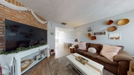 This three-floor home offers a well-organized layout with a variety of functional and comfortable living spaces throughout. The main living area features light blue-gray walls, wood-look flooring, and a charming brick accent wall housing a large flat-screen television. A white console table and plush brown sofas with soft pink accent pillows create a welcoming, casual atmosphere, while decorative wall hangings and warm lighting add personality to the space.

The kitchen is equipped with warm oak cabinetry, ample upper and lower storage, a double sink, dishwasher, and additional appliances. Adjacent to the kitchen, the dining area benefits from natural light pouring in through a sliding glass door that opens to an outdoor deck, with a pendant light fixture overhead completing the setting.

Multiple bedrooms are found across the floors, each carpeted and featuring windows that bring in natural light. One bedroom includes sliding glass door access to an outdoor staircase, while another serves a dual purpose as a study or creative workspace. A dedicated laundry room houses a full-sized washer and dryer with overhead wire shelving. The bathroom offers a wide vanity with ample counter space and a shower-tub combination.