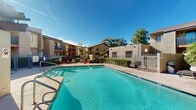 Located at 8603 N 22nd Ave in Phoenix, Arizona, this outdoor community space is designed to take full advantage of the region's abundant sunshine and warm climate. At its centerpiece is a generously sized swimming pool with clear, blue-green water, framed by a wide pool deck that provides ample room for lounging and relaxation. Entry steps with decorative tile detailing make for easy access into the water.

A standout architectural feature is the pergola shade structure positioned poolside, offering a covered gathering area furnished with outdoor seating — ideal for dining or socializing out of the direct sun. The surrounding buildings reflect a Southwestern-inspired design aesthetic, featuring stucco exteriors in warm earth tones, balconies with metal railings, and exterior staircases. Mature trees and well-maintained shrubs and greenery are thoughtfully integrated throughout the space, adding natural color and shade while softening the hardscape.

The pool area is enclosed by a metal security fence with gated entry, ensuring a safe and private environment. Outdoor lighting fixtures are positioned around the perimeter, extending the usability of the space into the evening hours. The overall ambiance is that of a relaxed, resort-style outdoor retreat well-suited to the Phoenix desert lifestyle.