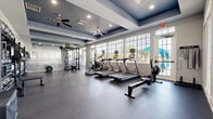 Located at 600 River Birch Ct in Clermont, FL, this fitness center offers a comprehensive workout environment within a single, open-plan space. The room features a striking tray ceiling with recessed lighting and deep navy-blue accents, creating a bold, modern aesthetic. Dual ceiling fans ensure consistent air circulation throughout the facility.

Large, multi-pane windows line one wall, inviting abundant natural light and providing views of the surrounding outdoor greenery. The durable dark rubber flooring spans the entire space, offering traction and impact absorption suitable for a wide range of exercises.

The facility is thoughtfully equipped with a diverse selection of cardio machines, including treadmills, an elliptical trainer, a stationary bike, and a rowing machine. A Rogue power rack with a barbell and weight plates supports strength training, while dedicated freeweight stations feature a full rack of dumbbells and kettlebells in multiple sizes. Medicine balls, resistance tools, and foam rollers round out the functional fitness offerings. Wall-mounted mirrors on one side of the room expand the sense of space and assist with form during workouts.

A posted set of gym rules ensures the facility remains organized and welcoming. The overall ambiance is clean, professional, and purposefully designed to support a full-spectrum fitness experience.