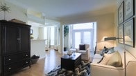 Located at 4055 Ridge Ave in the East Falls neighborhood of Philadelphia, PA, this single-floor residence offers a thoughtfully designed living space that balances comfort and style. The open-concept layout connects the living and adjoining areas seamlessly, creating a sense of spaciousness and easy flow throughout the home. The living room serves as the heart of the space, featuring warm hardwood flooring, crown molding, and neutral wall tones that lend a clean, sophisticated ambiance. A bold area rug and dark-finished furniture provide a striking contrast to the light surroundings. Large French doors and expansive windows flood the space with natural light, offering an inviting brightness throughout the day. The open pass-through to the kitchen area enhances the communal feel, making the space well-suited for entertaining. Architectural details such as decorative columns and defined archways add character and elegance to the interior. The overall aesthetic is polished yet welcoming, with a neutral palette that provides a versatile backdrop for a variety of design preferences. This well-appointed single-level home combines classic architectural charm with a bright, airy atmosphere in a convenient Philadelphia location.