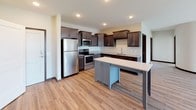 This single-floor residence offers a thoughtfully designed layout that balances functionality and modern aesthetics. The kitchen serves as a standout feature, showcasing rich dark-stained cabinetry with brushed nickel hardware, granite countertops, and a full suite of stainless steel appliances including a refrigerator, range, and built-in microwave. A contrasting light-colored island provides additional prep space and casual seating, while warm hardwood-style flooring and a tile backsplash complete the refined look.

The bedrooms are generously proportioned, each finished with plush neutral carpeting, dark wood baseboards, and ceiling fans with light fixtures. Several bedrooms benefit from large windows fitted with blinds, allowing ample natural light and views of surrounding greenery. The layout reveals multiple bedrooms, offering flexible living arrangements.

Both bathrooms maintain consistent finishes, featuring dark espresso cabinetry, granite-topped vanities, large framed mirrors, and hardwood-style flooring. One bathroom includes a tall linen tower cabinet for added storage, while both bathrooms are equipped with tub-shower combinations. Throughout the unit, neutral wall tones and cohesive dark trim create a clean, modern ambiance.