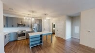 Located at 1941 Roland Clarke Place in Reston, VA, this well-designed 2-bedroom, 2-bathroom residence offers a thoughtful layout across a single floor. The open-concept living room greets you with warm hardwood-style flooring, a striking white brick accent wall, and floor-to-ceiling glass doors that flood the space with natural light and provide access to a private balcony with outdoor views.

The kitchen is a standout feature, showcasing gray shaker-style cabinetry with matte black hardware, quartz countertops, a classic white subway tile backsplash, stainless steel appliances, and a center island with pendant lighting — ideal for both everyday cooking and entertaining.

Both bedrooms are carpeted and bright, each benefiting from large windows with outdoor views. The primary bedroom is generously proportioned and includes a spacious walk-in closet outfitted with custom built-in shelving and dual hanging rods. The second bedroom features its own well-sized closet with wire shelving.

The primary bathroom impresses with a double-sink vanity, illuminated mirrors, wood-look flooring, and a separate glass-enclosed shower. The second bathroom mirrors the modern aesthetic with a tiled tub-shower combo, a quartz vanity, and an LED-backlit mirror. Clean lines and contemporary finishes are consistent throughout the entire residence.