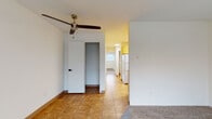 This single-floor residential unit offers a well-organized layout that balances functionality and comfort across its key living areas. The galley-style kitchen is outfitted with warm honey-toned wood cabinetry, granite-look countertops, a stainless steel sink, and white appliances including a refrigerator and electric range. Tile flooring runs through the kitchen and entry areas, providing easy maintenance in high-traffic zones. A hallway connects the kitchen to the rest of the unit, with a ceiling fan overhead adding air circulation to the transitional space. The living area is carpeted and benefits from a large window dressed with vertical blinds, allowing natural light to filter in while offering a view of the surrounding building exterior. A baseboard heating unit runs beneath the window, ensuring warmth throughout the space. The bedroom areas are finished with plush carpet and neutral white walls, creating a clean and versatile canvas. Closet access is available in the bedroom spaces. The bathroom features tile flooring, a wood vanity with a granite-look countertop, a framed mirror with overhead lighting, and standard fixtures. Overall, the unit presents a practical and move-in-ready layout with consistent finishes throughout.