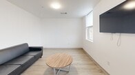 Located at 815 S Aurora St in Ithaca, NY, this three-bedroom, one-bathroom unit offers a clean, modern design spread across a single floor. The interior features a consistent palette of crisp white walls and light wood-look flooring in the main living areas, transitioning to patterned carpet in the bedrooms and hallways.

The kitchen is a standout feature, equipped with stainless steel appliances including a refrigerator, electric range, built-in microwave, and dishwasher. White shaker-style cabinetry and a bold yellow backsplash add a pop of color, while a dining area with natural light from nearby windows completes the space.

The living room is bright and functional, featuring a wall-mounted TV, a window with outdoor views, and light flooring that contributes to an airy atmosphere. A central hallway connects the living areas to the three bedrooms, each carpeted and sized to accommodate a bed, desk, and chair. The bedrooms include windows that bring in natural light and views of the surrounding greenery.

The shared bathroom is finished in the same clean, minimal aesthetic with light wood-look flooring and white walls. A central hallway with panel doors and an electrical panel provides practical access to all rooms, making the layout efficient and well-organized throughout.