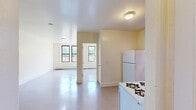 Located at 14 Bedell Street in Hempstead, NY, this single-floor unit offers two bedrooms, one bathroom, and a closet within a compact and efficiently arranged floor plan. The open kitchen and living area serves as the heart of the unit, featuring warm wood cabinetry, a white gas range, a refrigerator, and a sink set beneath a window that brings in natural light. The speckled terrazzo-style flooring in this area adds a classic touch to the space.

The spacious primary bedroom is a standout feature, offering generous room to accommodate a variety of furniture arrangements. Both bedrooms are finished with neutral carpet flooring and crisp white walls, and each is equipped with a baseboard heating unit. Windows in both bedrooms frame views of the surrounding greenery, filling the rooms with natural light and a sense of openness.

The bathroom is clean and functional, featuring white tile flooring, a tub-shower combination, a vanity with wood cabinetry, and a window for ventilation and light. Throughout the unit, clean white walls, bright finishes, and a straightforward layout create a simple, livable environment well-suited for everyday comfort.