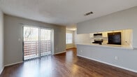 This two-story home in Austin, TX offers a functional and well-organized layout across two floors. The main level features an open-concept living and kitchen area with durable hardwood-style flooring throughout. The living room is anchored by a classic dark brick fireplace and is bathed in natural light through large sliding glass doors with vertical blinds that open to an outdoor view. The kitchen is defined by a peninsula counter with white cabinetry, an electric range, and an adjacent dining nook with a bright window — ideal for everyday meals. A conveniently located half bathroom completes the main floor. Upstairs, two carpeted bedrooms provide comfortable retreats, each with ceiling fans and private access to their own bathrooms. The primary bedroom includes an en-suite bathroom featuring a wide white quartz vanity, ample cabinetry with matte black hardware, and a large mirror. A walk-in closet adds practical storage. The second bedroom also benefits from its own bathroom and a dedicated closet. Throughout the home, a neutral gray and white color palette creates a clean, cohesive aesthetic, while textured ceilings and consistent trim work add a finishing touch to each space.