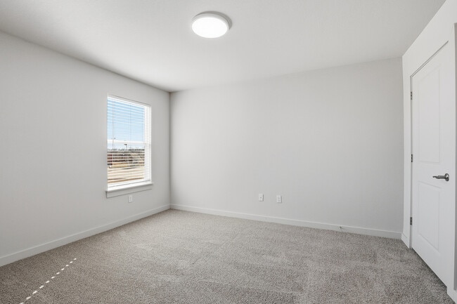 Bright and airy room with plush carpeting, large window allowing natural light, and modern white walls. - Oaks at Mustang