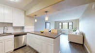 Located on the 12th floor at 735 SW Saint Clair Ave in Portland, Oregon, this one-bedroom, one-bathroom unit offers a well-designed layout that maximizes its compact footprint. The open-concept living and kitchen area is anchored by a modern kitchen featuring white shaker cabinetry, quartz countertops, stainless steel appliances, and pendant lighting above a breakfast bar with seating — ideal for casual dining. The living area is bathed in natural light through large windows that frame views of the surrounding cityscape and greenery, with warm-toned walls and wood-style flooring contributing to a clean, inviting atmosphere. The bedroom is a comfortable retreat, appointed with plush carpeting, a built-in wardrobe with paneled doors, and a window that continues to bring in natural light and urban views. The bathroom is finished with neutral tile wainscoting, a tub-shower combination, and classic white fixtures that give it a tidy, timeless feel. Throughout the unit, the neutral color palette and consistent design choices create a cohesive and functional living space suited for urban living in the heart of Portland.