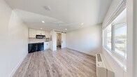 Located at 615 Jawdin Ave in Richland, Washington, this single-floor studio unit offers an efficiently designed layout that makes excellent use of its compact footprint. The main living area features light-toned wood-look plank flooring and crisp white walls illuminated by recessed lighting, creating a clean, modern atmosphere. A large window near the entry door allows natural light to fill the space while offering views of the surrounding neighborhood.

The kitchenette is neatly tucked into one corner and includes white shaker-style cabinetry, a geometric tile backsplash, a black over-the-range microwave, a sink, and a black compact refrigerator — providing all essential cooking amenities in a streamlined footprint.

A standout feature of the unit is the sliding barn door with a black metal rail, which opens to a fully tiled bathroom. The bathroom showcases hexagonal white mosaic wall tile and a bold navy and white star-patterned floor tile, lending a distinctive, designer touch. The bathroom includes a toilet, sink, and a walk-in shower with brushed nickel fixtures.

A wall-mounted HVAC unit ensures year-round climate comfort. The overall design balances functionality with modern aesthetic details, making this an efficient and visually appealing space in Richland, WA.