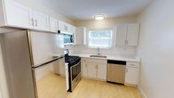 This two-bedroom residence spans two floors, offering a practical and well-appointed layout designed for comfortable everyday living. The main level features a bright, updated kitchen outfitted with crisp white shaker-style cabinetry, white quartz-style countertops, and a classic subway tile backsplash. Stainless steel appliances — including a gas range, built-in microwave, refrigerator, and dishwasher — provide a full suite of modern conveniences. A window above the sink allows natural light to fill the space, creating a clean and airy atmosphere. Light wood-tone flooring runs throughout the main level, contributing to the home's fresh, contemporary feel. The living area is open and welcoming, highlighted by sliding glass doors with vertical blinds that provide both natural light and direct access to the exterior. A carpeted staircase with sleek black metal railings connects the two floors, offering a defined transition between the main living spaces below and the private quarters above. The overall ambiance of this residence is clean, functional, and move-in ready, with thoughtful finishes that balance style and practicality throughout both levels.
