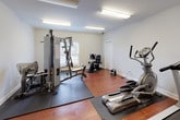 Located at 100 Estella Ct in Florence, Alabama, this single-floor fitness center is a well-equipped exercise facility designed to support a comprehensive workout routine. The space features warm hardwood-style flooring throughout, crisp white walls, and bright overhead fluorescent lighting that ensures excellent visibility across the entire room.

The cardio area is equipped with multiple treadmills and elliptical trainers, each placed on protective rubber mats, along with a stair stepper and a wall-mounted television for entertainment during workouts. On the strength training side, a large multi-function cable and weight machine takes center stage, accompanied by a recumbent stationary bike and additional resistance equipment, providing options for a full-body strength regimen.

Natural light filters in through windows fitted with white horizontal blinds, adding a bright and open feel to the space. Protective rubber floor mats are strategically placed beneath the heavier equipment to preserve the flooring and provide stability. A yoga mat is also available for stretching and floor exercises. The room includes a dedicated door for entry and exit, and a paper towel dispenser is mounted on the wall for convenience. The overall layout is organized and spacious, allowing multiple users to exercise comfortably at the same time.