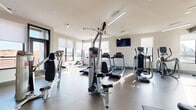 Located at 1414 Broadview Ave in Columbus, Ohio, this well-equipped fitness center offers a comprehensive workout environment spread across a single open floor. The space is designed with functionality and comfort in mind, featuring bright white walls, durable flooring, and an abundance of natural light streaming through multiple large windows fitted with roller shades.

The cardio zone is outfitted with Matrix treadmills, elliptical trainers, stationary bikes, and a WaterRower rowing machine, all arranged to take advantage of the surrounding views of the Columbus skyline. Ceiling fans provide additional ventilation throughout the space.

The strength training area includes a Hoist multi-functional cable machine, a dedicated free weight section with a full rack of dumbbells, and an adjustable workout bench positioned on protective floor mats. Flat-screen televisions are mounted on the walls for entertainment during workouts.

A mirrored studio area, separated by floor-to-ceiling glass partitions, provides an open, reflective space ideal for stretching, yoga, or group exercise. This section is stocked with stability balls and additional accessories stored on organized racks. Structural columns with contrasting dark accents contribute to the modern architectural design of the space, while ceiling fans and recessed lighting ensure a comfortable and well-lit environment throughout.