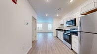 This single-floor unit presents a clean, contemporary design characterized by an open-concept layout that seamlessly connects the kitchen and living areas. The kitchen is well-appointed with a full suite of stainless steel appliances, including a Whirlpool refrigerator, electric range, over-the-range microwave, and dishwasher. White shaker-style cabinetry provides generous storage, complemented by dark granite countertops that offer a striking visual contrast. A stainless steel sink with a modern faucet completes the functional workspace.

Light hardwood-style flooring flows consistently throughout the unit, enhancing the sense of openness and continuity. Recessed lighting illuminates the kitchen and main living area, while neutral white walls create a bright, versatile backdrop. The living area benefits from natural light through multiple windows, lending an airy quality to the space.

The bedroom is a well-proportioned, quiet retreat featuring multiple windows with blinds and the same consistent flooring. It includes access to a dedicated walk-in closet equipped with wire shelving systems for organized storage. An additional room, also with natural light and recessed lighting, provides further flexible living or sleeping space. Overall, the unit offers a fresh, move-in-ready environment with modern finishes throughout.