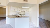 Located at 5200 Coe Ave in Seaside, California, this 2-bedroom, 2-bathroom residence offers a well-organized single-floor layout designed for comfortable everyday living. The open living area is highlighted by soaring vaulted ceilings and an elegant chandelier, creating a bright and airy atmosphere. Sliding glass doors lead to a private balcony, filling the space with natural light and providing outdoor access. The kitchen is efficiently designed with white cabinetry, granite-style countertops, a gas range, a refrigerator, and a skylight overhead. A peninsula with bar-height seating connects the kitchen to the living area, making it ideal for casual dining and entertaining. Both bedrooms feature plush carpeting, natural light from window blinds, and dedicated closet spaces. The primary bedroom includes a walk-in closet with built-in shelving. Each of the two bathrooms is equipped with a full tub-shower combination, accented by clean white and gray tile surrounds with chrome fixtures. Soft carpet continues throughout the bedrooms and living areas, while the kitchen features tile-style flooring. A hallway connects the private quarters, completing this thoughtfully arranged and functional floor plan.
