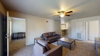 This single-story unit offers a thoughtfully arranged layout designed for comfortable everyday living. The living area serves as the central gathering space, featuring warm carpet flooring, a ceiling fan with integrated lighting, and a front entry door flanked by windows that allow natural light to filter in. The space flows openly toward the dining and kitchen area, which is separated by a raised bar counter with pendant lighting overhead and barstool seating — ideal for casual dining or entertaining.

The kitchen is galley-style, featuring warm wood cabinetry, dark countertops, tile flooring, and a full suite of black appliances including a refrigerator, range, microwave, and dishwasher. Recessed and pendant lighting illuminate the workspace effectively.

The bedrooms are carpeted and equipped with ceiling fans and natural light from exterior-facing windows. Each room offers a functional and quiet retreat. The unit includes two bathrooms, both finished with tile flooring, wood vanity cabinetry, dark countertops, and a large mirror. One bathroom features a full tub-shower combination.

A dedicated in-unit laundry area houses a full-sized washer and dryer, adding everyday convenience. Wire shelving above the appliances provides additional storage.