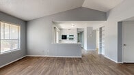 This single-story unit offers a thoughtfully arranged floor plan that maximizes its comfortable footprint. The open-concept living area immediately impresses with vaulted ceilings that create a sense of spaciousness, neutral gray walls, and wood-look hard flooring that flows consistently throughout the main areas. A bank of three windows along the living room's far wall floods the space with natural light, while a second window on the adjacent wall enhances the bright, airy feel.

The kitchen is separated from the living area by a half-wall breakfast bar and features white cabinetry with modern hardware, light quartz-style countertops, a classic subway tile backsplash, and a full suite of black appliances including an electric range, refrigerator, and dishwasher. A window above the sink adds natural light to the cooking space.

The bedroom is comfortably sized, finished with plush carpet, a ceiling fan, and multiple windows that bring in natural light. Built-in shelving near the entrance provides practical storage. The bathroom includes a white vanity with a quartz-style countertop, a large mirror, and a full tub-shower combination, all finished with the same wood-look flooring found throughout the unit.