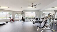 This fitness center offers a comprehensive workout environment designed to accommodate a wide range of exercise needs. The space is thoughtfully laid out across a single floor, with durable rubber flooring throughout that provides both safety and comfort during workouts.

The cardio zone features multiple treadmills and an elliptical trainer, each positioned to take advantage of the large windows that line the walls, offering pleasant outdoor views of the surrounding greenery. A wall-mounted flat-screen television adds entertainment options for cardio sessions.

The strength training area is well-appointed with a multi-station cable machine, a dedicated weight bench, and a full rack of dumbbells ranging across various weights, catering to both beginner and advanced users. A spin bike and a balance trainer further diversify the available workout options.

Full-length mirrors along one wall enhance the sense of openness while allowing users to monitor their form during exercises. Multiple ceiling fans are evenly distributed throughout the space, ensuring consistent air circulation and comfort. Bright, even lighting complements the natural light streaming through the large windows.

Additional amenities include a sanitation station with wipes and dispensers, a water station, and a private restroom accessible from within the fitness center, making this a fully self-contained and practical facility.