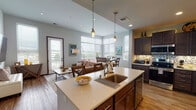 Located at 220 W Main St in downtown Waukesha, Wisconsin, this well-appointed single-floor residence offers a thoughtfully designed open-concept layout that seamlessly connects the kitchen, dining, and living areas. The kitchen is a standout feature, showcasing rich dark cabinetry, stainless steel appliances, a mosaic tile backsplash, and a large center island with light quartz countertops, pendant lighting, and a double-basin sink — ideal for both everyday cooking and entertaining. The dining area is bathed in natural light through large windows fitted with horizontal blinds, offering pleasant views of the surrounding Waukesha cityscape. The living room continues this bright, airy feel with direct access to an outdoor space via a glass-panel door, wood-look flooring, and ample room for comfortable seating. The bedrooms are generously proportioned, featuring plush carpeting and large windows that invite natural light and outdoor views. The bathrooms are finished with warm travertine-style tile flooring, dark wood vanities, quartz countertops, and well-lit mirrors. Throughout the residence, a neutral color palette and consistent use of dark wood accents create a cohesive, modern aesthetic that is both functional and welcoming.