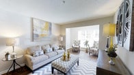 This well-appointed 1-bedroom, 1-bathroom residence is thoughtfully designed across a single floor, offering a comfortable and cohesive living experience. The living area serves as the heart of the home, featuring hardwood-style flooring and a seamless open layout that connects the main seating area to a sun-filled sitting nook. A large window dressed with classic white shutters allows generous natural light to pour in, creating a warm and airy ambiance. The neutral color palette — anchored by soft greige walls and a textured ceiling — provides a versatile backdrop that complements a range of design styles. The space flows naturally from one area to the next, offering defined zones for relaxation and conversation without sacrificing openness. A bold abstract wall accent adds a touch of contemporary artistry, while layered lighting enhances the overall warmth of the interior. The combination of clean architectural lines, tasteful finishes, and abundant natural light gives this residence a polished yet inviting character, making it an ideal space for comfortable everyday living.
