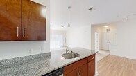 This single-floor residence features 2 bedrooms and 2 bathrooms within a thoughtfully designed layout. The kitchen serves as a central highlight, boasting rich dark-wood cabinetry extending to the ceiling for ample storage, granite countertops, stainless steel appliances including a refrigerator, range, and over-the-range microwave, and a kitchen island with an integrated sink and pendant lighting above. Wood-look flooring runs throughout the kitchen, which opens seamlessly toward the living area. The living room is carpeted and filled with natural light from a large sliding glass door dressed with vertical blinds, creating a bright and airy atmosphere. Both bedrooms are carpeted and offer a comfortable sense of space; one bedroom includes a closet with built-in rod shelving. The primary bedroom is generously sized. The two bathrooms are finished consistently with granite-topped vanities and rich wood cabinetry. One bathroom features a glass-enclosed walk-in shower, while the second includes a full soaking tub with a shower combination and a curved curtain rod. Tile flooring completes both bathrooms. The overall aesthetic is clean and modern, with neutral tones throughout creating a cohesive and inviting environment.