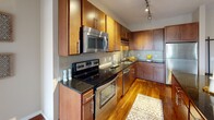 This single-floor residence showcases a thoughtfully designed open-concept layout that seamlessly connects the kitchen, dining, and living areas. The kitchen is well-appointed with warm-toned wood cabinetry, dark granite countertops, a subway tile backsplash, and a full suite of stainless steel appliances including a range, built-in microwave, dishwasher, and refrigerator. Track lighting overhead provides focused illumination throughout. A kitchen island with bar seating extends the workspace and creates a natural transition to the living area.

The living room is bright and inviting, benefiting from large sliding glass doors that open to a private balcony, allowing abundant natural light and outdoor views. Rich hardwood flooring runs throughout the main living spaces, adding warmth and continuity to the design.

The bathroom features dark granite vanity countertops paired with rich wood cabinetry, a large mirror, and clean tile flooring. A second bathroom offers a similarly refined vanity setup with consistent finishes. The generously sized walk-in closet includes multiple wire shelving systems, offering ample storage and organization capacity. Overall, the space presents a clean, contemporary aesthetic with consistent, quality finishes throughout.