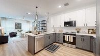 Located at 505 W 8th St in Dallas, TX, this thoughtfully designed one-bedroom, one-bathroom residence offers a modern aesthetic and efficient use of space across a single floor. The open-concept living, dining, and kitchen area serves as the heart of the home, featuring light wood-style flooring and an abundance of natural light from large windows dressed in neutral linen curtains. The kitchen is a standout, showcasing two-tone cabinetry—white upper cabinets paired with gray lower cabinets—complemented by a herringbone tile backsplash, quartz countertops, stainless steel appliances, and a peninsula with bar seating illuminated by sleek pendant lights. The living area provides a warm, inviting atmosphere with ample room for comfortable furnishings. The bedroom is a serene retreat with large windows, plush carpeting, and direct access to multiple closets. The full bathroom impresses with its elongated double-vanity, white shaker cabinetry, black hardware accents, large wall mirrors, and a full tub with shower. In-unit laundry and four closets add notable practicality. The overall design balances contemporary style with functional comfort throughout.