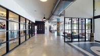 Located at 1600 NW 17th Ave in Miami's dynamic Allapattah district, this single-floor amenity space blends industrial design with vivid local art to create an energetic, community-focused environment. Polished concrete floors run throughout, complemented by exposed ductwork overhead and black pendant lighting that reinforce the building's industrial-chic aesthetic.

The main open corridor and lounge area is anchored by a striking colorful mural column and a bold "MIAMI"-themed graffiti wall that pays homage to the city's street art culture. Black steel-framed glass partitions divide the space into distinct zones while maintaining visual openness and allowing natural light to pour in through floor-to-ceiling windows along the perimeter.

A spacious social lounge features a full-size pool table, high-top seating, and leather lounge chairs, all framed by large windows with views of the surrounding neighborhood. Adjacent to this is a well-appointed communal kitchen with custom cabinetry, herringbone tile backsplash, a stainless steel refrigerator, a center island with bar seating, and industrial-style pendant lighting.

A dedicated fitness center, accessible through glass-panel doors, is adorned with its own graffiti mural and equipped with workout stations. An elevator provides convenient access, and the overall design reflects a bold, Miami-inspired identity with strong artistic character throughout.