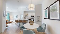 This single-story residence is thoughtfully designed with a seamless open-concept layout that connects the living, dining, and kitchen areas into one cohesive, light-filled space. Light wood-style flooring flows throughout the main living areas, complemented by a neutral palette of soft whites and grays that lend an airy, contemporary feel.

The kitchen is well-appointed with white shaker cabinetry extending to the ceiling, granite countertops, a classic white subway tile backsplash, and a full suite of stainless steel appliances including a range, microwave, dishwasher, and side-by-side refrigerator. A peninsula with bar seating provides additional workspace and casual dining options. Pendant lighting accents the kitchen and dining area, where a round white table with soft teal velvet chairs anchors the space beneath a statement drum pendant light.

The living room offers a relaxed, comfortable atmosphere with neutral furnishings and direct access to adjacent spaces. The bedrooms feature plush carpet, large sliding glass doors that invite natural light and outdoor views, and generous proportions. The bathrooms are finished with granite-topped white vanities, wood-look flooring, and clean, modern fixtures. A built-in wall niche adds a subtle architectural detail throughout the unit.