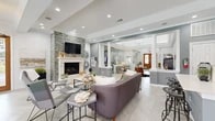 This single-story community clubhouse is designed with a sophisticated yet welcoming aesthetic throughout. The grand entrance lobby sets the tone with soaring tray ceilings, a statement globe chandelier, herringbone-patterned light stone flooring, and decorative columns that define the space without obstructing sightlines. A cowhide rug and live-edge accent table add organic warmth to the airy entryway.

The open lounge area flows naturally from the lobby and serves as the social heart of the space. A stacked stone accent wall frames a classic fireplace with a white mantel and mounted flat-screen television, while plush seating invites relaxation. Recessed lighting and crown molding enhance the refined atmosphere.

Adjacent to the lounge is a fully functional kitchen featuring rich dark wood cabinetry, quartz countertops, a mosaic tile backsplash, stainless steel appliances, and a central island with bar seating — ideal for community gatherings and events.

The business center offers a quiet, carpeted workspace with a built-in desk, overhead cabinetry, and generous natural light from large windows with wood blinds. A dedicated fitness center, enclosed by floor-to-ceiling glass walls, is outfitted with cardio machines, strength training equipment, free weights, medicine balls, and exercise balls beneath a tray ceiling with a ceiling fan.