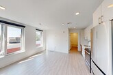 Located at 42 N Beacon Street in Boston's Allston neighborhood, this thoughtfully designed one-bedroom, one-bathroom unit offers a clean, modern aesthetic throughout. Light wood-toned flooring flows continuously across the entire space, complementing the crisp white walls and recessed lighting that create a bright, airy atmosphere.

The entrance hall leads into an open-concept living area bathed in natural light from large windows fitted with roller shades. The galley-style kitchen is well-appointed with high-gloss white cabinetry, quartz countertops, a white subway tile backsplash, stainless steel appliances including a range, microwave, refrigerator, and dishwasher, and a single-basin sink with a modern pull-down faucet. A wall-mounted mini-split unit provides efficient climate control.

The bedroom features two corner-positioned windows that invite ample natural light and offer views of the surrounding neighborhood streetscape. A double-door closet provides dedicated storage space. The bathroom is finished with large-format tile flooring, full subway tile surround in the soaking tub and shower combination, a wood-toned vanity with a white countertop, and a wide mirror with contemporary lighting. The unit presents a cohesive, move-in-ready design throughout.