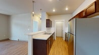 Located at 16511 East Sprague Avenue in Spokane Valley, WA, this single-floor unit features a thoughtfully designed open-concept layout that seamlessly connects the kitchen, dining, and living areas. The kitchen is a standout feature, boasting rich dark-espresso cabinetry, light countertops, stainless steel appliances including a full-size refrigerator and range, a peninsula with pendant lighting overhead, and warm wood-look flooring that extends throughout the main living space. A dedicated in-unit laundry closet with a stacked washer and dryer is conveniently located adjacent to the kitchen. The spacious living room is filled with natural light from multiple windows and a glass-paneled entry door, creating a bright and welcoming atmosphere. The bedroom offers plush carpeting, a generous window with neighborhood views, and access to a closet with built-in shelving. The bathroom features a dark-toned vanity with chrome hardware, mosaic tile backsplash accents, and a mirrored medicine cabinet. Additional storage is available throughout the unit. Baseboard heating is present in key areas, ensuring year-round comfort. The overall design balances modern aesthetics with functional living, making this a practical and attractive space.