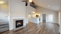 This two-story residence offers a thoughtfully designed layout with a striking open-concept main living area at its heart. The vaulted ceiling soars dramatically overhead, complemented by a ceiling fan and a gas fireplace with a clean white mantel, creating a warm and airy atmosphere. Rich hardwood-style flooring extends throughout the main level, and large windows flood the space with natural light and outdoor views. The kitchen features a galley-style configuration with white quartz countertops, modern flat-front cabinetry, stainless steel appliances including a built-in microwave, dishwasher, and refrigerator, plus a mosaic tile backsplash for a contemporary touch. A convenient peninsula connects the kitchen to the living area. The bathrooms are finished with sleek dark cabinetry, white quartz vanity tops, light tile flooring, and chrome fixtures. One bathroom includes a tub-shower combination with floor-to-ceiling tile surround. A dedicated laundry area houses a full-size washer and dryer. Upstairs, carpeted bedrooms offer comfortable retreats, with one bedroom featuring dual closets for ample storage. A carpeted staircase with a handrail connects both floors, completing this well-appointed home.