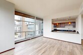 This thoughtfully designed 2-bedroom, 2-bathroom residence delivers a refined living experience through a cohesive blend of modern finishes and functional layout. The open-concept living and kitchen area serves as the heart of the home, anchored by expansive floor-to-ceiling windows with sliding glass access that flood the space with natural light and frame sweeping urban views. Light-toned hardwood flooring runs throughout the main living areas, complementing the clean, neutral palette of the walls and trim.

The kitchen is a standout feature, showcasing rich wood cabinetry, dark granite countertops, stainless steel appliances, and a breakfast bar illuminated by warm pendant lighting — ideal for both everyday meals and entertaining. The bathrooms echo this refined aesthetic with granite vanity tops and wood cabinetry.

Both bedrooms are carpeted for comfort, offering a quiet retreat from the main living areas. The spacious primary bedroom includes a closet with built-in shelving. Dark-framed interior doors and dark baseboards provide a sharp contrast against the light walls throughout, adding a contemporary edge. A dedicated in-unit laundry room with full-size washer and dryer adds everyday convenience, completing this well-rounded residence.