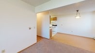 Located at 3100 33rd St S in Fargo, North Dakota, this single-floor unit offers a practical and well-organized layout suited for comfortable everyday living. The spacious living area features neutral-toned carpet, baseboard heating, and multiple windows dressed with vertical blinds, allowing natural light to fill the room. A wall-mounted air conditioning unit provides additional climate control. The layout transitions seamlessly from the living area into the galley-style kitchen, which is equipped with warm wood cabinetry, white appliances including an electric range, microwave, and refrigerator, a single-basin sink, and easy-to-clean tile flooring. The kitchen also provides a direct sightline to the rest of the unit, enhancing the open feel of the space. Multiple bedrooms are present, each featuring plush carpet, baseboard heating, and windows with vertical blinds that offer privacy while still admitting natural light. The bathroom is finished with tile flooring, a vanity with an integrated sink, a large mirror, wood-framed cabinetry for storage, and clean white fixtures. Throughout the unit, the design is clean and neutral, offering a move-in ready environment with consistent finishes and functional amenities.